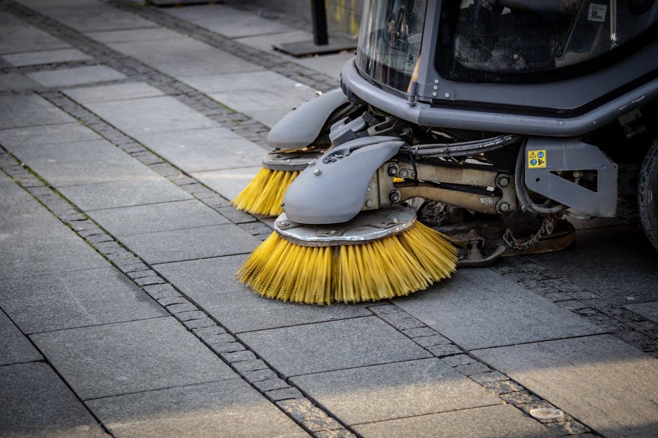 Close-up view of a road sweepers yellow brushes on a paved street.